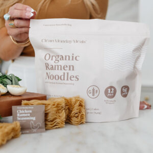 Bag with ramen blocks and seasoning packets in front, near cutting board in kitchen.